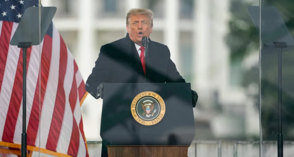 Donal Trump speaking at podium next to American flag