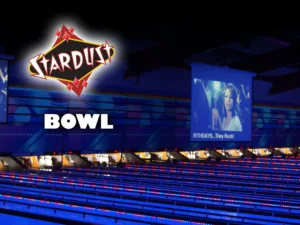 A bowling lane with a big screen TV, lit up at night for glow bowling.