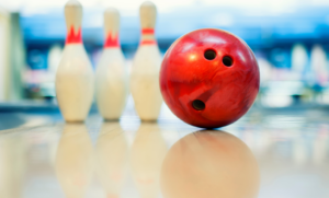 A red bowling ball and three bowling pins sitting on a well-lit alley.