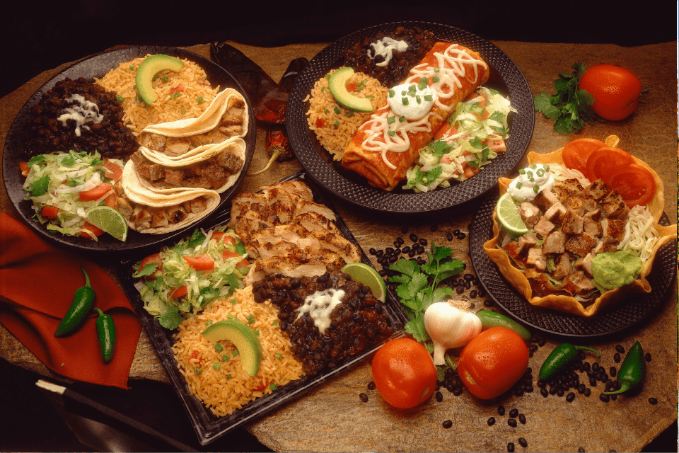 An array of dishes in a Mexican restaurant including a wet burrito, tacos, and rice and beans.