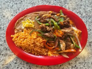 A steak fajita bowl served in a red bowl with rice and beans.