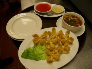 A table with several dishes: crab cheese wontons, hot and sour soup, and some accompanying sauces.