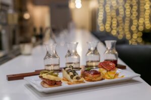 A flight of wine carafes sitting in front of a rectangular plate with small bites.