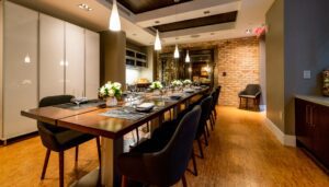 A long dining table set with flowers and place settings in front of a wine wall.