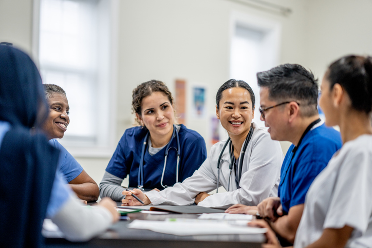 nurses and doctors sit around a table with folders on the table.