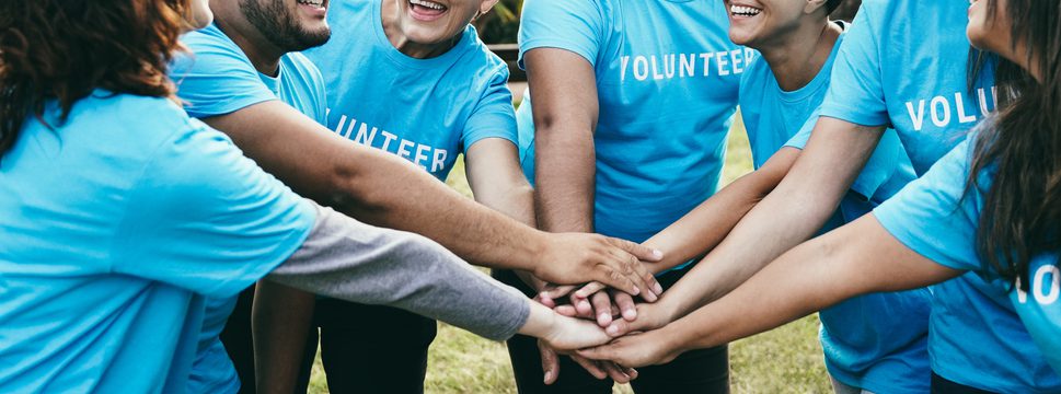 Happy group of volunteer people stacking hands celebrating together outdoor. There are plenty of great volunteer opportunities in Detroit.