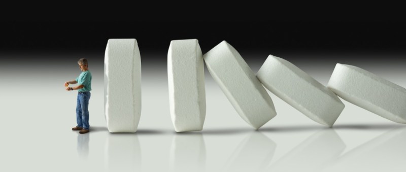 Impending doom and demise of man with pharmaceutical opioid pain medication addiction represented by huge row of pills crashing over like dominoes to eventually crush the man.