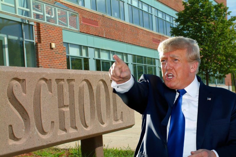 Trump infront of Large School sign in front of school building.