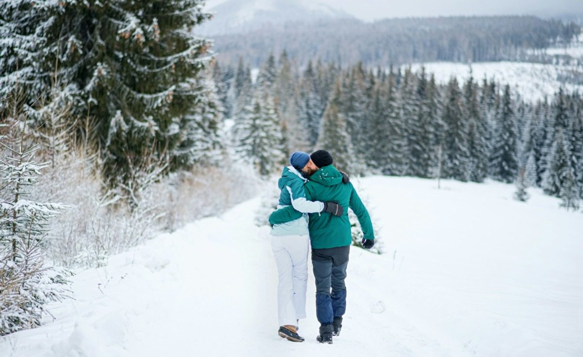 A couple holding each other and walking down a snowy mountain slope.