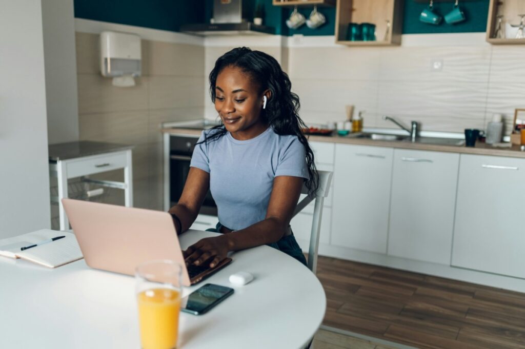 Young black woman typing at her laptop and smiling.