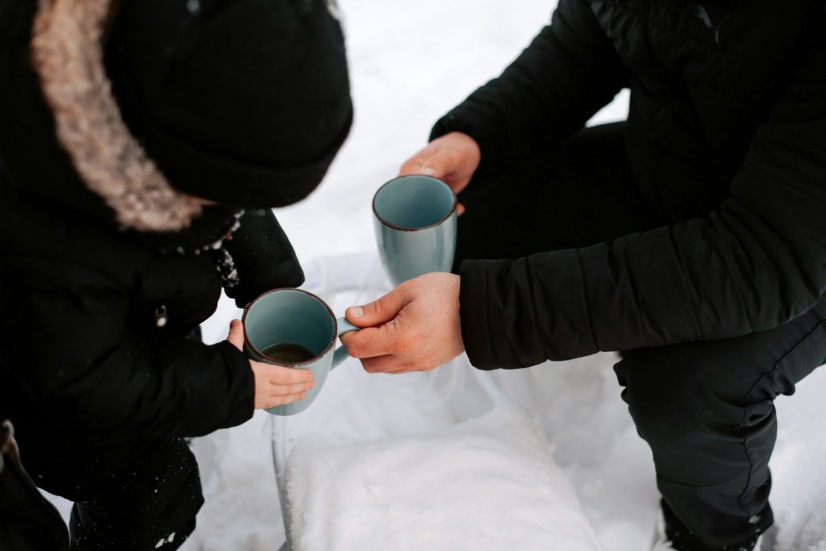 Two people wearing all black holding two coffee cups.