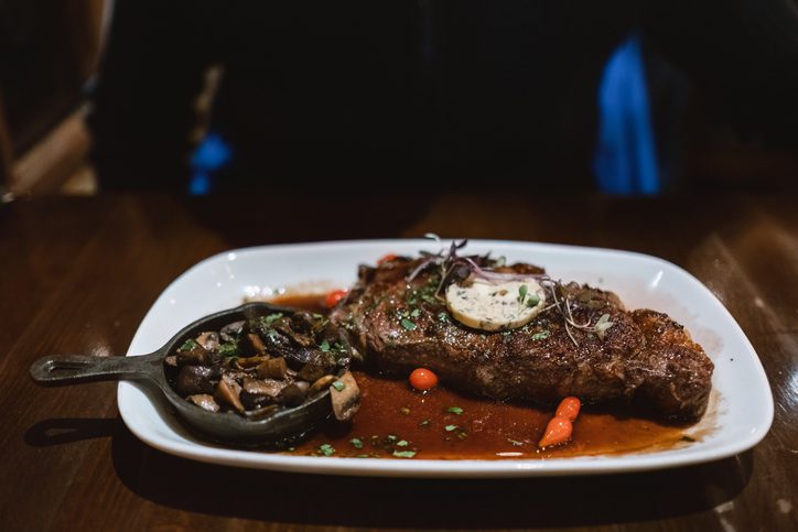 Close-up of ribeye steak and side of mushrooms on plate at restaurant