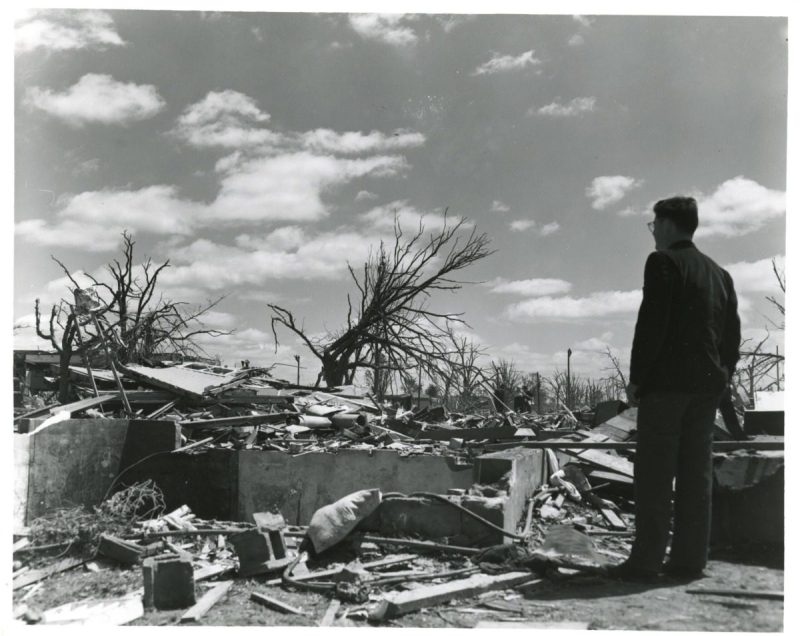 a black and white photo of a man looking out over tornado damage