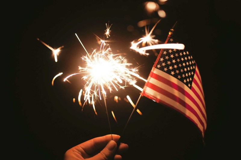 A hand holds an American flag and a sparkler